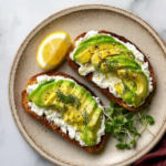 Cottage Cheese Avocado Toast: Quick, Creamy, High-Protein Breakfast 5 Cottage cheese avocado toast served with lemon and microgreens on ceramic plate.